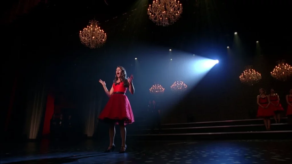 Rachel Berry con i palmi delle mani verso l'alto mentre canta in una delle sue migliori interpretazioni di Glee